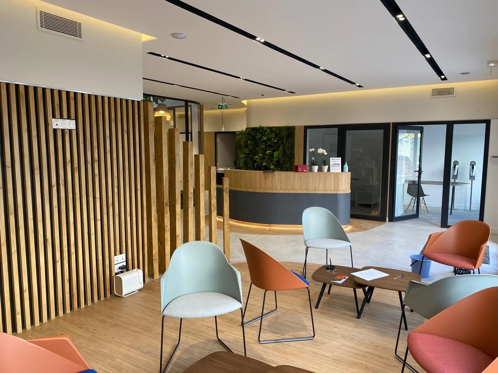 Espace d’attente avec assises colorées, claustra en bois et vue sur le comptoir d’accueil