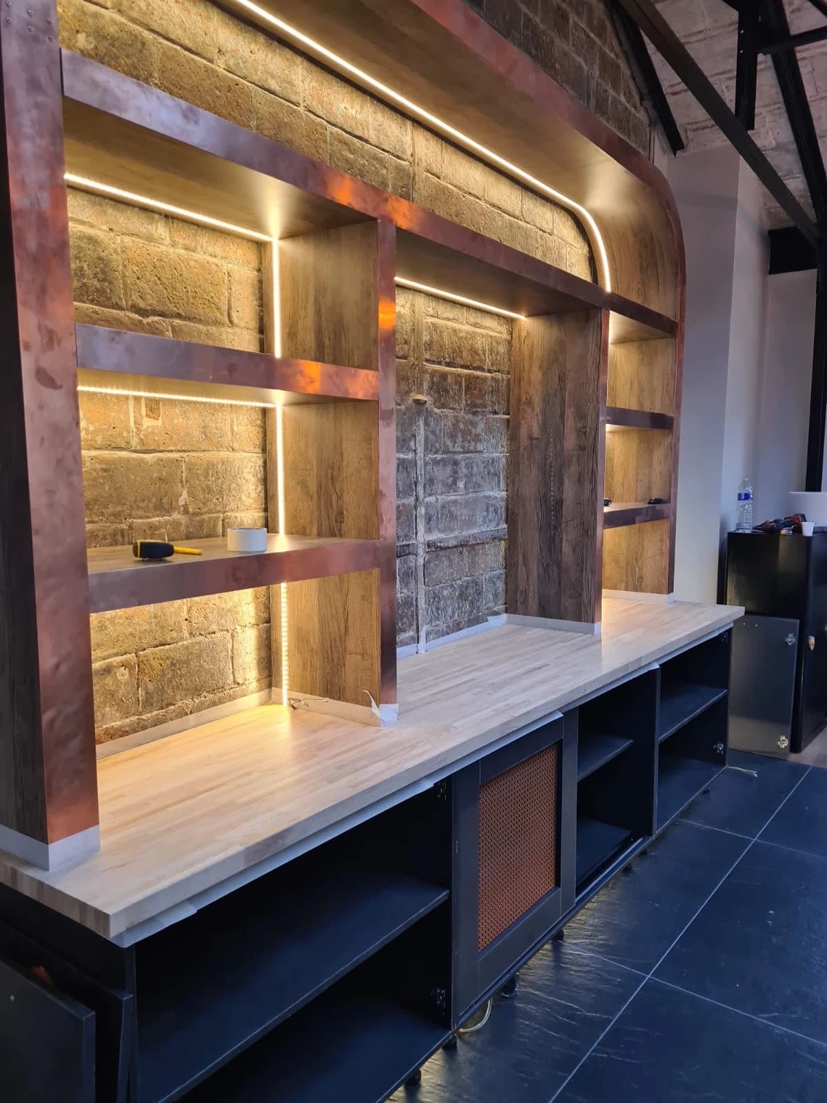 Détail des étagères rétroéclairées et du revêtement cuivré derrière le bar