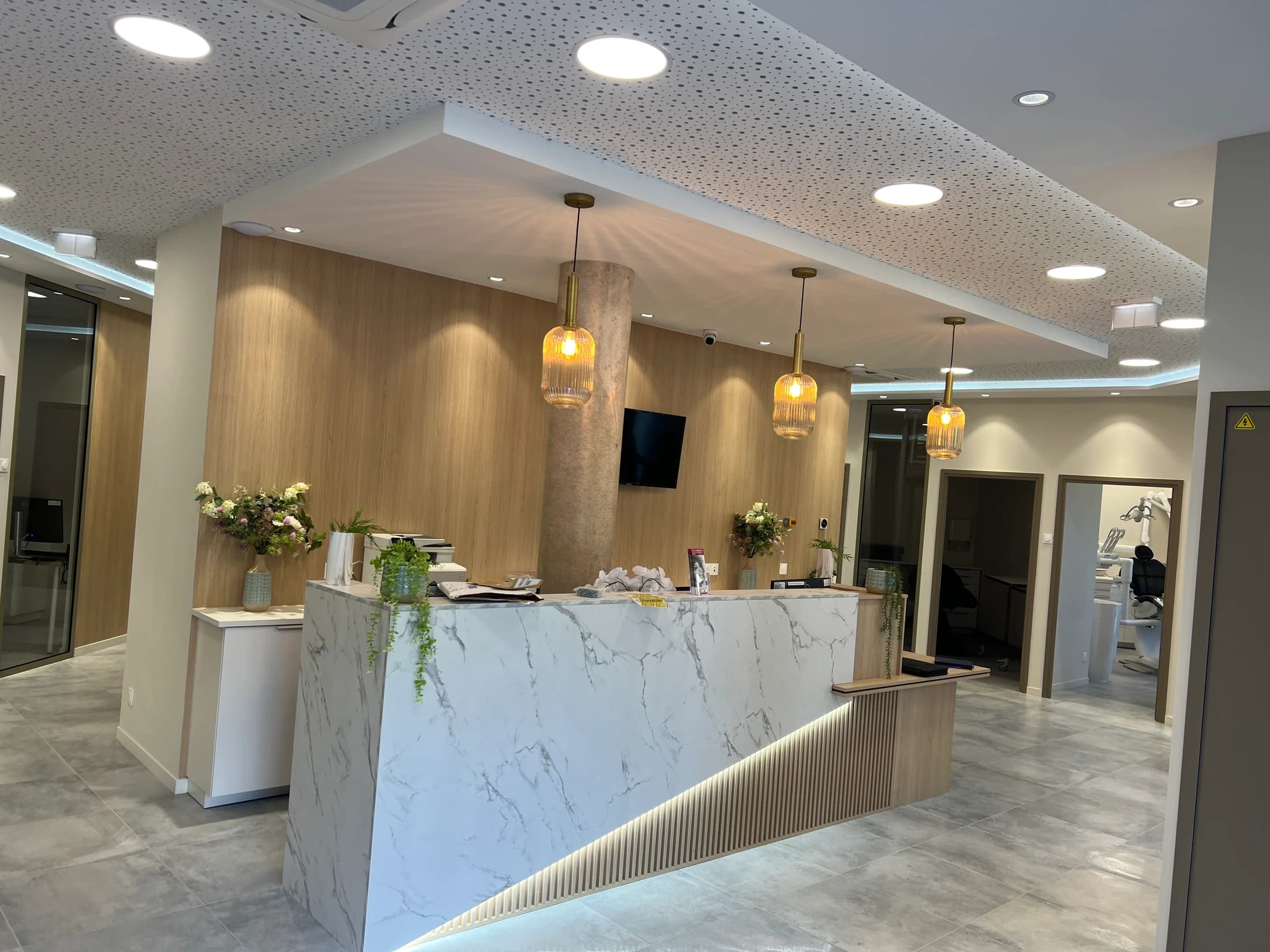 Photo réelle de la réception avec comptoir effet marbre, bois cannelé et suspensions dorées